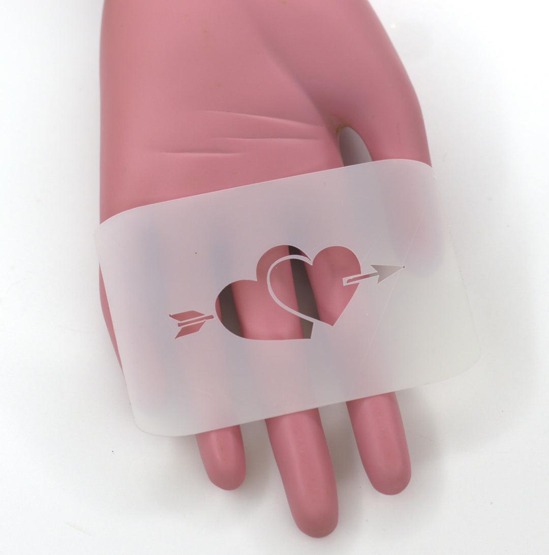 two heart with arrow through cut on plastic pet as a stencil held on pink plastic fake hand
