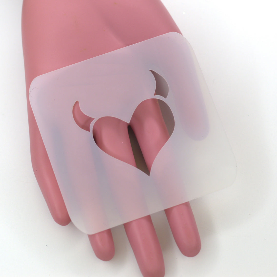 plastic white stencil of heart with devil bull horns held by pink hand