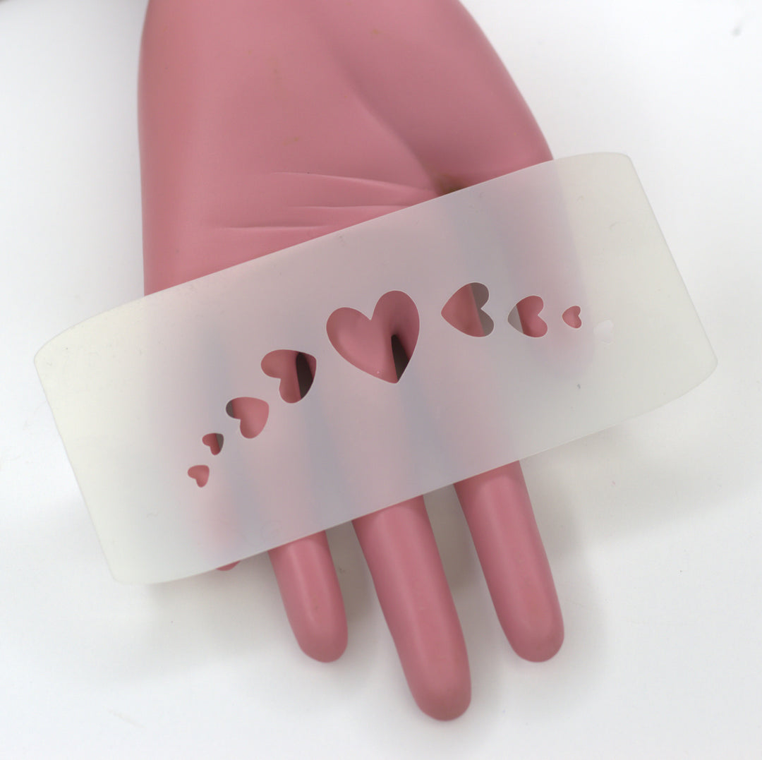 white plasic stencil of a heart with sideways hearts on the side held by pink hand