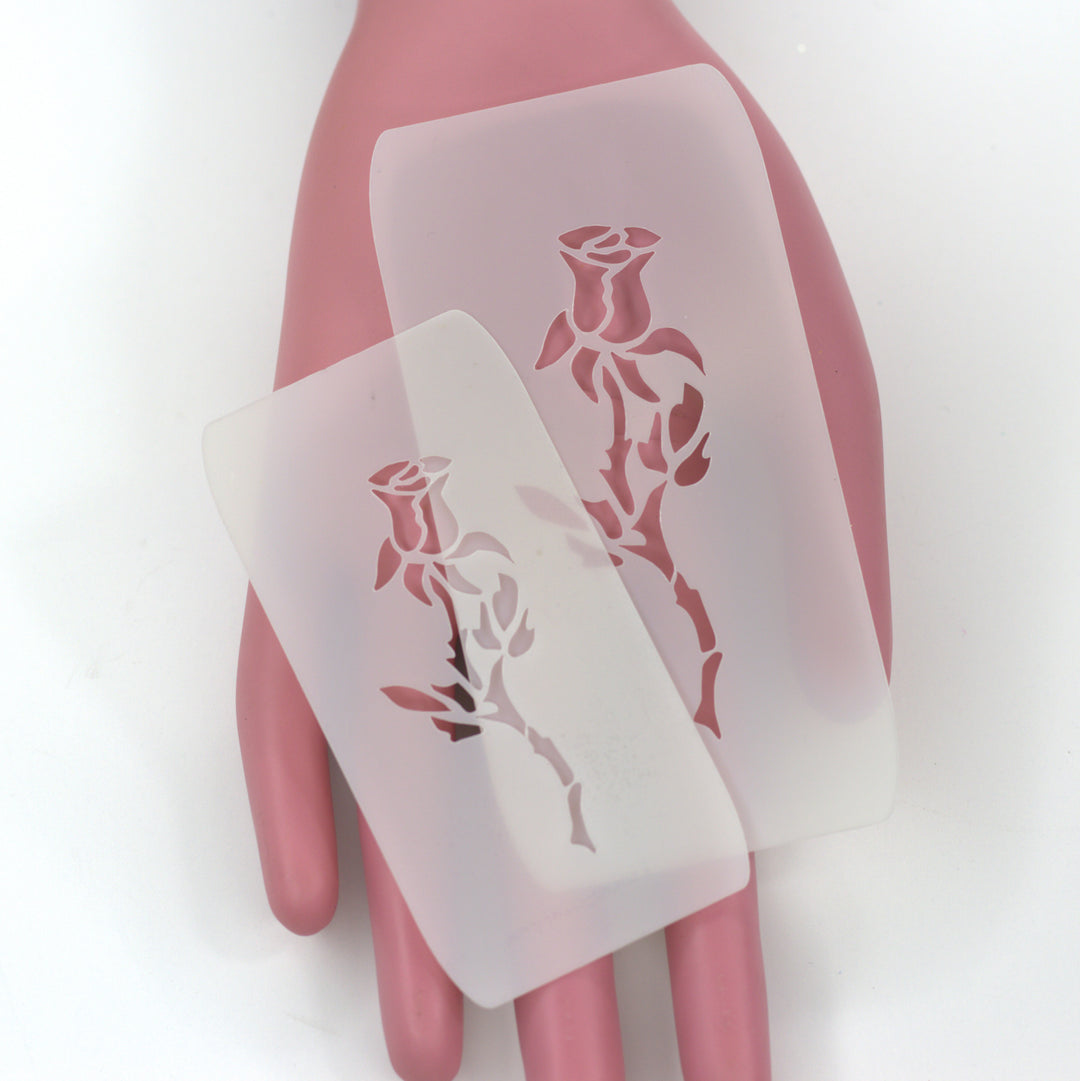 two translucent white stencils of long sten rose buds on a plastice pink hand