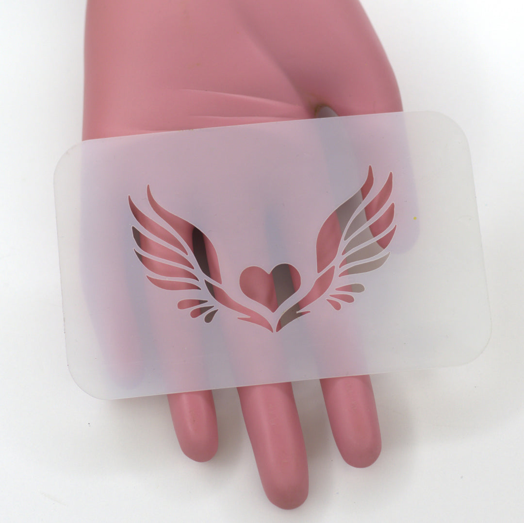 plastic stencil of a small heart with detailed wings held by plastic pink hand