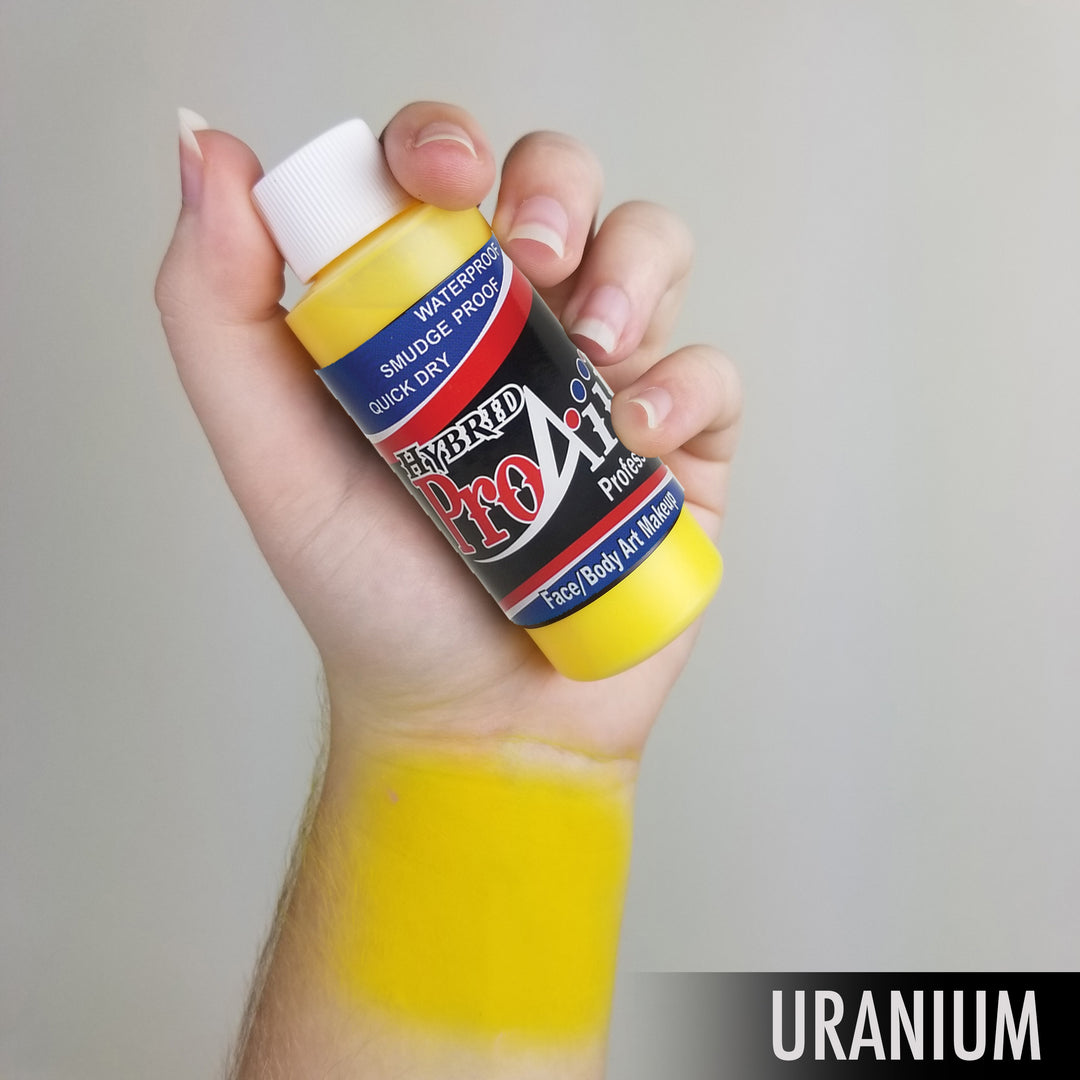 Hand holding bottle of proaiir brand face body airbrush paint with swatch of color on arm uranium yellow